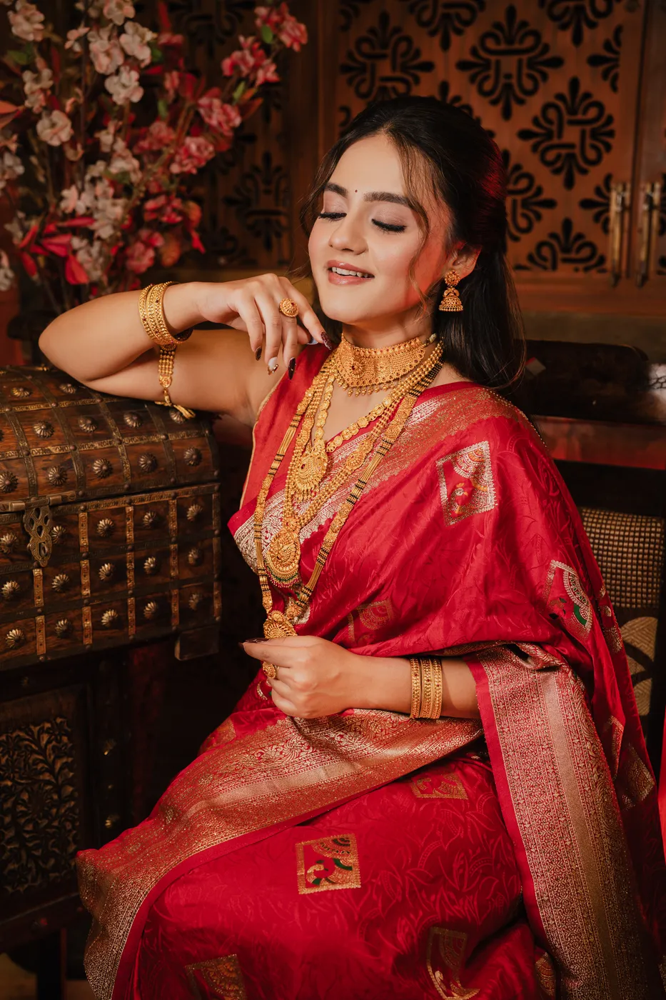Model wearing traditional gold jewellery from Baba Jewellers, leaning on a carved wooden chest