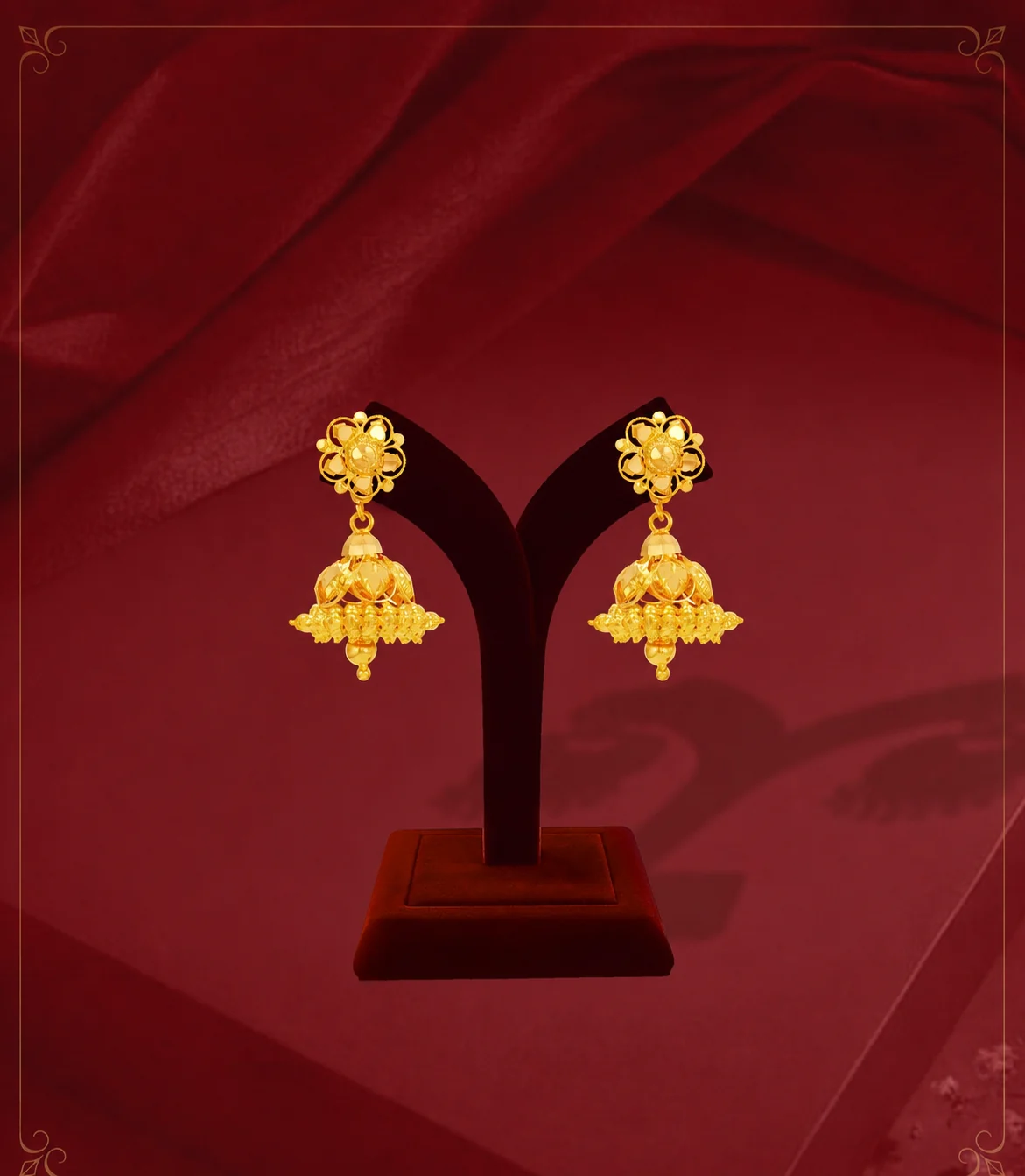 Traditional gold jhumka earrings hanging on a display stand