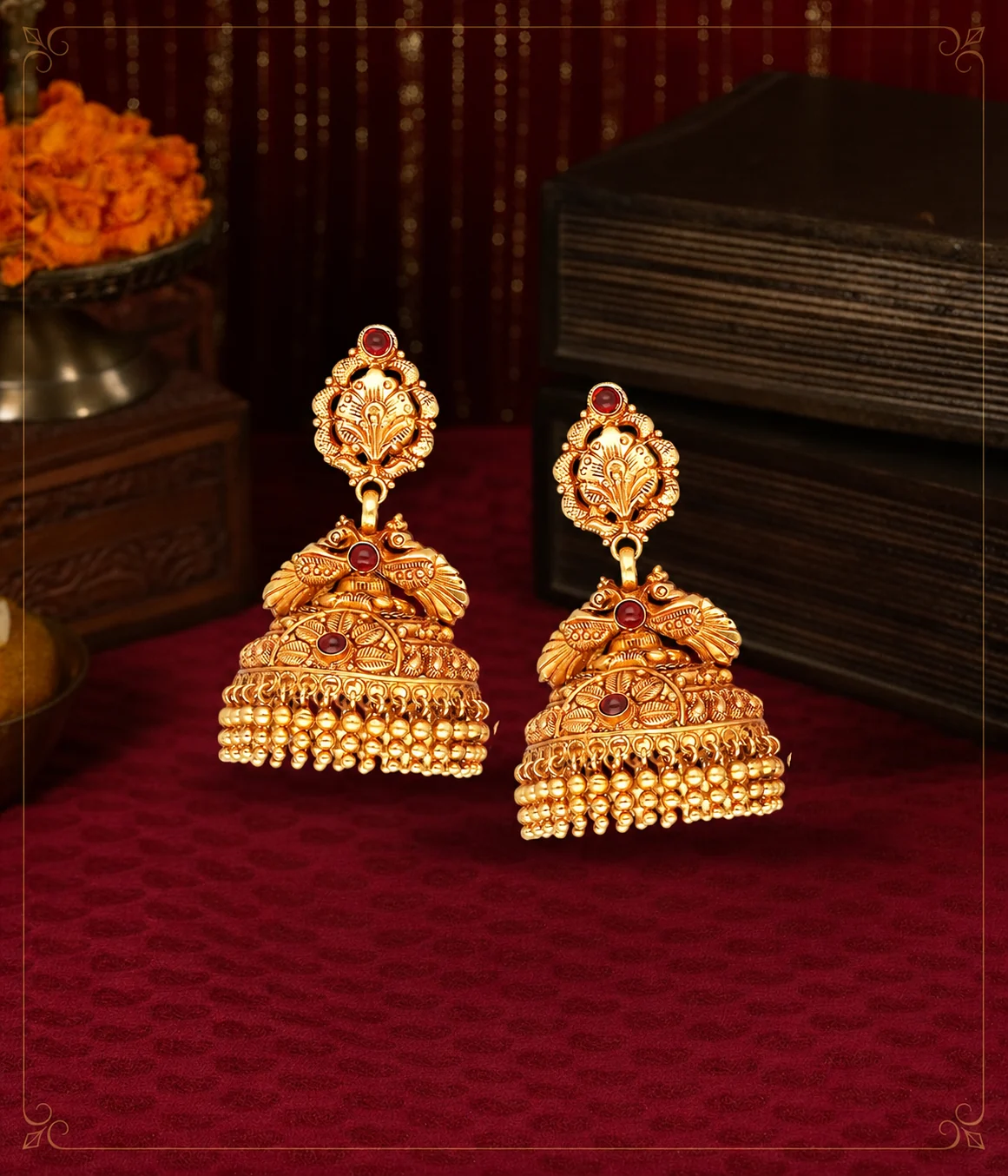 Ornate gold jhumka earrings photographed on deep maroon velvet